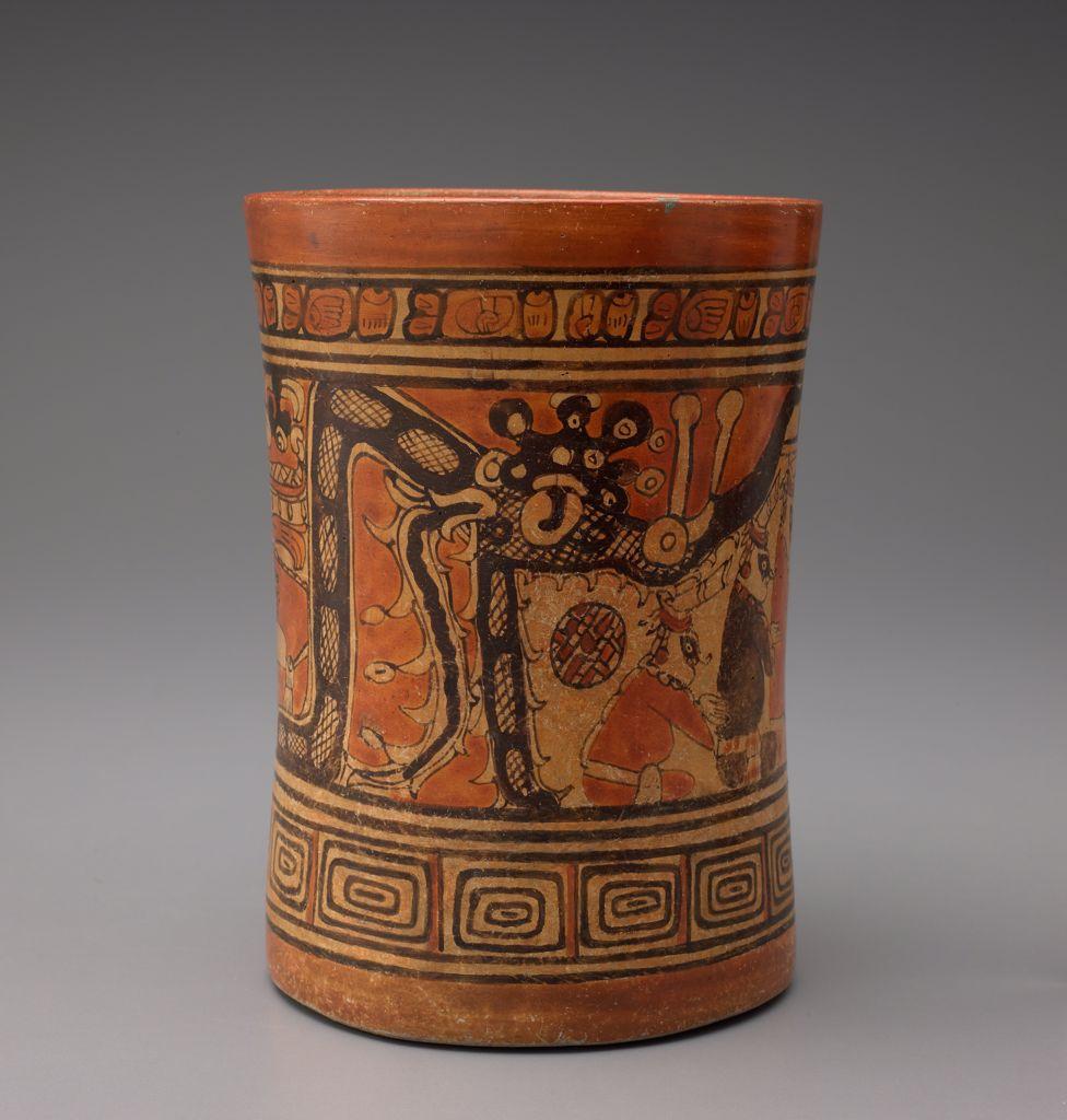 A ceramic vase depicting a dragon-like animal preparing to eat a stylized human figure. The design is framed by repeating geometric motifs.